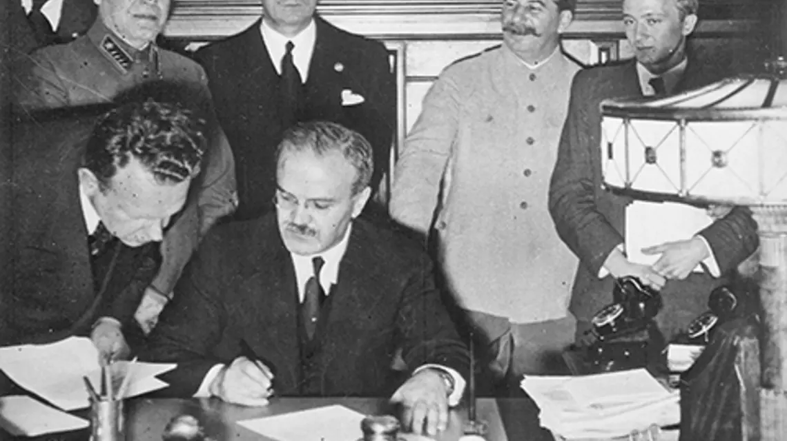 Przewodniczący Rady Komisarzy Ludowych Wiaczesław Mołotow składa podpis pod paktem, z tyłu stoją Joachim von Ribbentrop i Józef Stalin, Moskwa, 23.08. 1939 r. | fot. NAC