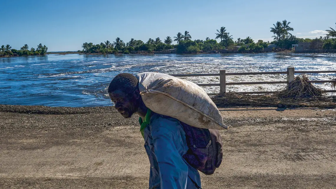 Katastrofalna powódź w Mozambiku, która dotknęła ponad 100 tys. osób, odcięła kluczowe szlaki transportowe i utrudnia dostawy pomocy humanitarnej. Na zdjęciu mieszkaniec miasta Xai-Xai z paczką żywnościową na zniszczonym moście nad rzeką Limpopo, 5 lutego 2026 r. fot. Zinyange Auntony/AFP/East News